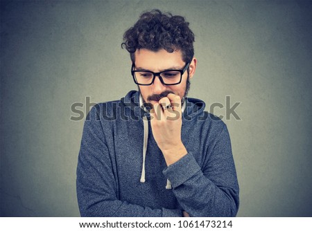 Closeup portrait nervous man biting fingernails craving something and anxious on gray wall background. Negative human emotion facial expression perception