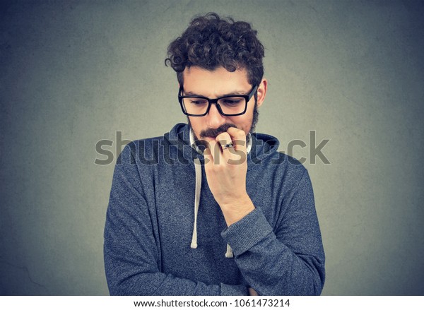 Closeup portrait nervous man biting\
fingernails craving something and anxious on gray wall background.\
Negative human emotion facial expression\
perception
