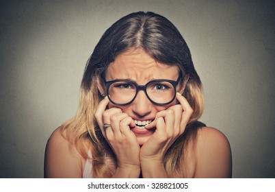 Closeup portrait nervous stressed young woman girl in glasses student biting fingernails looking anxiously craving something isolated on grey wall background. Human emotion face expression feeling