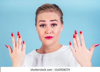 Close-up Portrait Of Nervous Unhappy Young Blonde Woman Looking At A Broken Fingernail And Crying . Red Long Nails Manicure Broken Nail Blue Background In Studio