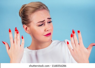 Close-up Portrait Of Nervous Unhappy Young Blonde Woman Looking At A Broken Fingernail And Crying . Red Long Nails Manicure Broken Nail Blue Background In Studio