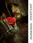 Close-up portrait of a noble knight in armor with a red rose in his hands. The era of romanticism. 