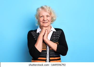 Closeup portrait of old beautiful woman smiling,keeping plams under her chin over isolated blue background,close up portrait. studio shot.beauty, plan, idea, woman thinking about her happy youth.
