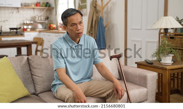 closeup portrait of old male asian dementia patient\
sitting alone with a stick and blank expression on face in the\
living room at home