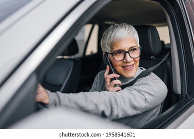 Close-up Portrait Of An Older Woman Driving A Car And Talking On Smart Phone.