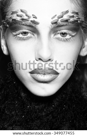 Closeup portrait of one beautiful wild young woman with bright animal makeup with thorns on face on studio background black and white, vertical picture