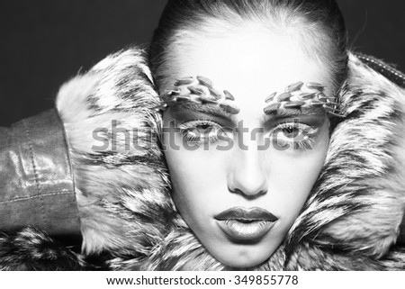 Closeup portrait of one beautiful wild young woman with bright animal makeup with thorns on face in fur coat in studio black and white, horizontal picture