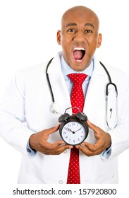 Closeup Portrait Of An Overwhelmed, In A Hurry, Busy, Unhappy Male Doctor Holding An Alarm Clock Running Out Of Time Isolated On A White Background. Health Care Reform, Medicaid Reimbursement. 