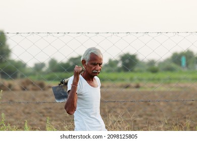 Close-up Portrait Photo Of An Senior Male Indian Farmer Standing In The Field At Sunset With A Shovel On His Shoulder And Wore A White Vest