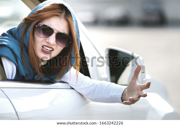 Closeup portrait of pissed off\
displeased angry aggressive woman driving a car shouting at someone\
with hand fist up. Negative human expression\
consept.