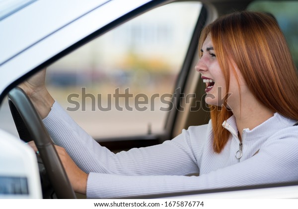 Closeup portrait of pissed off\
displeased angry aggressive woman driving a car shouting at someone\
with hand fist up. Negative human expression\
consept.