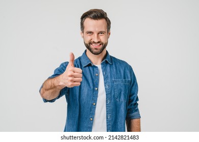 Closeup Portrait Of Positive Caucasian Young Man In Denim Casual Clothes Showing Thumb Up For Good Quality Checkup, Smiling With Toothy Smile Isolated In White Background