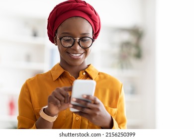 Closeup portrait of positive stylish young black lady in red turban using modern smartphone, SMM-manager chatting with clients or posting content, working online, panorama with copy space - Powered by Shutterstock