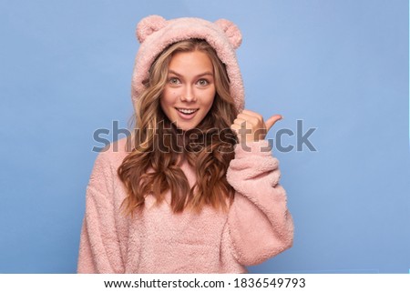 Close-up portrait of a pretty attractive beautiful rather surprised cheerful cheerful girl pointing her fingers ad advertising advice decision to copy space in pink clothes bear on a blue background
