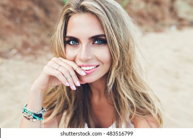 Closeup portrait of pretty blonde girl with long hair and blue eyes posing on rocky beach. She is smiling to the camera.