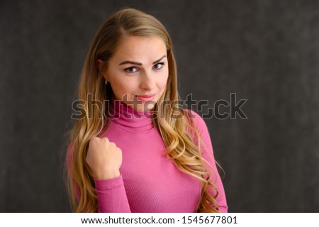 Close-up portrait of a pretty blonde girl with long curly hair standing in the studio on a gray background with emotions in different poses in a pink sweater. Beauty, Model, Cosmetics