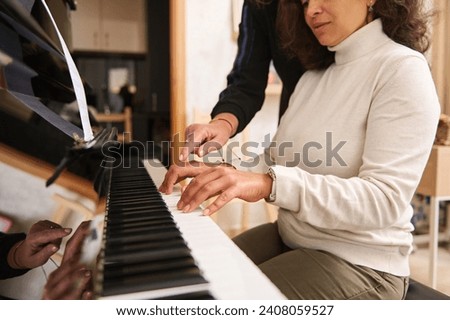 Close-up portrait of pretty young adult Latin American woman learning playing grand piano with her teacher, a talented pianist musician during music class. People. Arts. Culture. Lifestyle. Education