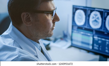 Close-up Portrait Of Professional Doctor Looking At MRI Or CT Scan Images On His Computer Monitor, Searching For Signs Of Brain Tumor Or Cancer, Trying To Diagnose Disease.