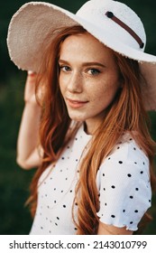 Close-up portrait of redheaded woman with freckled skin and long hair, wearing hat, posing outdoor. Beauty fashion model. Beauty skin female face. Elegant style