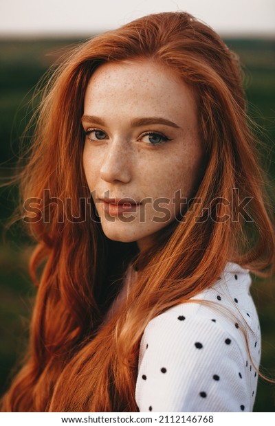 Close-up portrait of a redheaded\
woman with freckles looking at camera while posing outdoor. Natural\
beauty concept. Beautiful girl. Pretty young woman.\
Outdoor