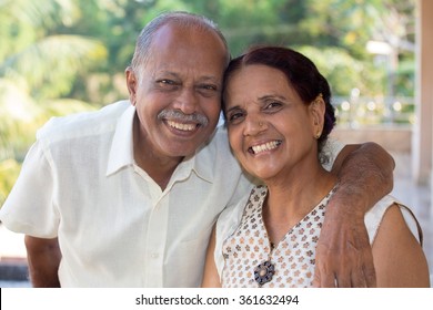 Closeup portrait, retired couple in white shirt and dress holding each other smiling,enjoying life together, isolated outside green trees background.