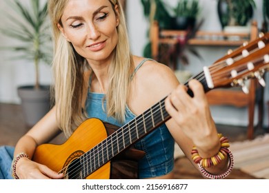 Close-up Portrait Of Romantic Blond Young Woman Playing Acoustic Guitar Sitting On The Floor