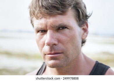 Closeup Portrait Of Rugged Caucasian Man With Stern Bold Facial Expression, Distinct Features, And Intense Predator Eyes In Undefined Outdoor Environment