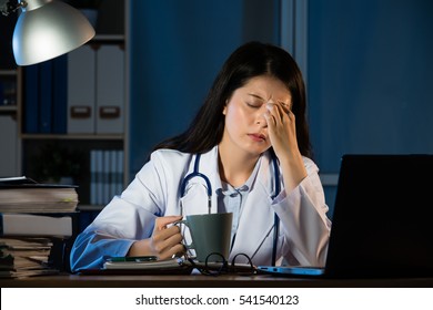 Closeup Portrait Sad Unhappy Health Care Professional With Headache Stressed Sleepy Holding Cup Of Coffee. Nurse Doctor With Migraine Overworked Overstressed. Pretty Mixed Race Asian Chinese Woman