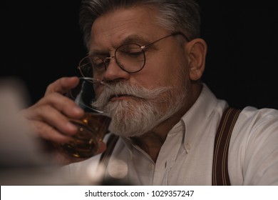 Close-up Portrait Of Senior Man Drinking Whiskey On Black