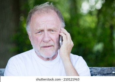 Closeup Portrait, Senior Mature Man In White T-shirt Sitting On Bench, Having Serious Conversation On Cell Phone, Isolated Outside Outdoors Background