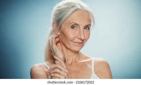 Close-up Portrait Of Senior Woman Looking At Camera, Touching Hair, Beautiful Face, Smiling. Elderly Lady With Natural Grey Hair, Blue Eyes. Beauty, Dignity, Grace Of Old Age. Abstract Blue Background