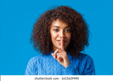 Close-up Portrait Sensual And Mysterious African-american Woman With Cute Happy Smile, Shushing, Press Index Finger To Lips Having Secret, Prepare Surprise And Hush Looking Camera, Blue Background