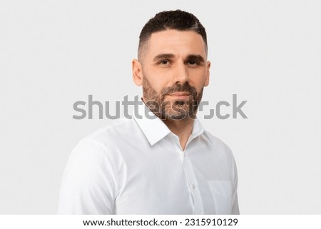 Closeup portrait of serious european middle aged man wearing shirt posing looking at camera over light studio background. Male self confidence concept