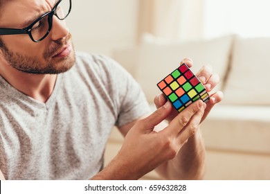 Close-up portrait of serious young man in eyeglasses holding rubik cube