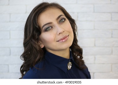 Closeup portrait of a serious young woman smiling, against a white brick wall, summer indoors.