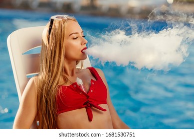 Close-up Portrait of sexy young (vaping) girl. Female smoke e-cigarette on sunbed near the pool. Vapor concept.