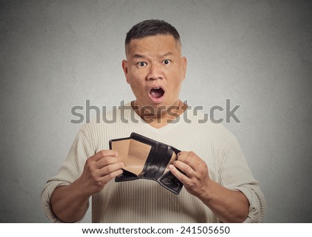 Closeup portrait shocked puzzled unhappy business man worker employee, funny looking guy, student, holding empty wallet isolated grey wall background. Bankruptcy financial difficulty. Face expressions