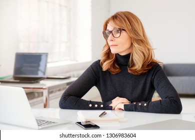 Close-up portrait shot of attractive businesswoman looking thoughtfully while sitting at office desk behind her laptop.  - Shutterstock ID 1306983604