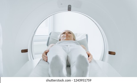 Close-up Portrait Shot Of A Female Patient Lying On A CT Or MRI Scan, Bed Is Moving Inside The Machine While It Scans Her Body And Brain. In Medical Laboratory With High-Tech Equipment.