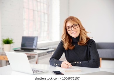 Close-up portrait shot of middle aged businesswoman wearing casual clothes while sitting at office desk and doing some paperwork.