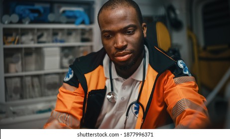 Close-up Portrait Shot Of A Serious And Focused Black African American Paramedic Providews First Aid To An Injured Patient In An Ambulance Vehicle. Emergency Medical Technician Is Checking Up Patient