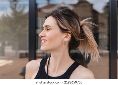 Close-up portrait shot of a young blonde business lady with a hair claw in her straight hair. Woman standing near business centre building and look at side with a style hairstyle, earrings.
