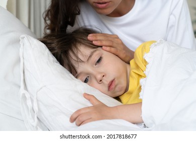 Closeup Portrait Of Sick Kid Lying In Bed With Worried Mom On Bedside Comfort Child Suffering From Fever Or Flu. Female Parent Caring Of Exhausted Toddler Boy. Toddler Sickness And Home Cure Concept