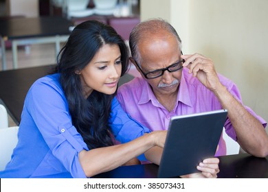 Closeup portrait, sitting young woman showing elderly with black glasses to use portable device,scrutinizing data with great concern, isolated indoors background - Powered by Shutterstock