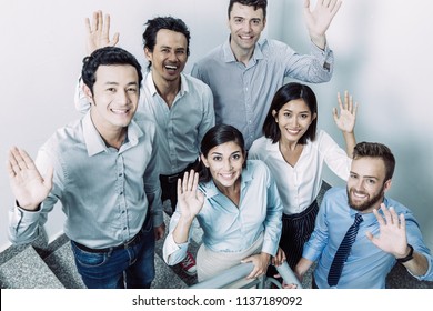 Closeup Portrait Of Six Joyful Middle-aged Business People Gathering On Office Stairway, Standing, Looking At Camera And Waving With Hands. High Angle View.