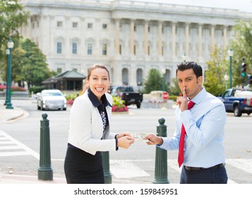 Closeup Portrait Of Sleazy Businessman Or Lobbyist Offering Money Dollars Bribe And Saying Shhh To Happy Corrupt Politician In Washington Dc, Isolated On Capitol Building Background