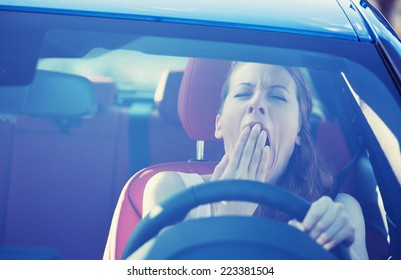 Closeup portrait sleepy tired fatigued exhausted young attractive woman driving her car in street traffic after long hour trip windshield front view. Transportation sleep deprivation accident concept