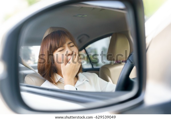 Closeup portrait sleepy, tired young woman\
driving her car after long hour trip in mirror, Sleep deprivation,\
accident concept