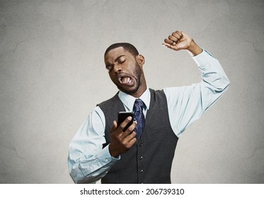 Closeup Portrait Sleepy Young Business Man, Funny Guy Stretching, Yawning, Looking At Smart Phone Being Bored By Phone Conversation, Texting Isolated Black Background. Facial Expression, Body Language