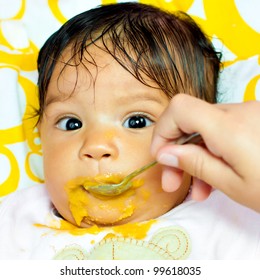 Close-up Portrait Of A Small Hispanic Baby Girl Eating Her Meal And Making A Mess